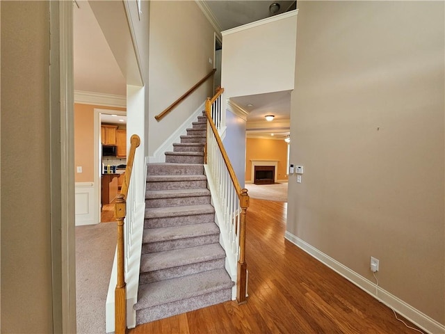 stairway with wood finished floors, a ceiling fan, a fireplace, crown molding, and baseboards