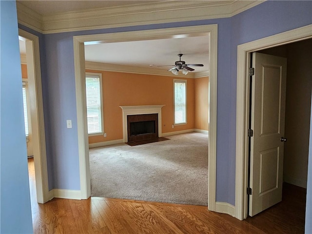 unfurnished living room with baseboards, ornamental molding, a fireplace with flush hearth, and a ceiling fan