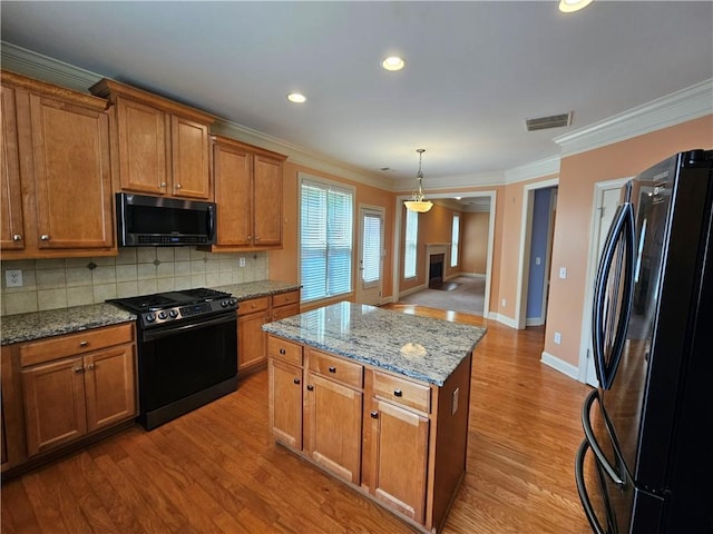 kitchen featuring brown cabinetry, ornamental molding, black appliances, visible vents, and decorative backsplash