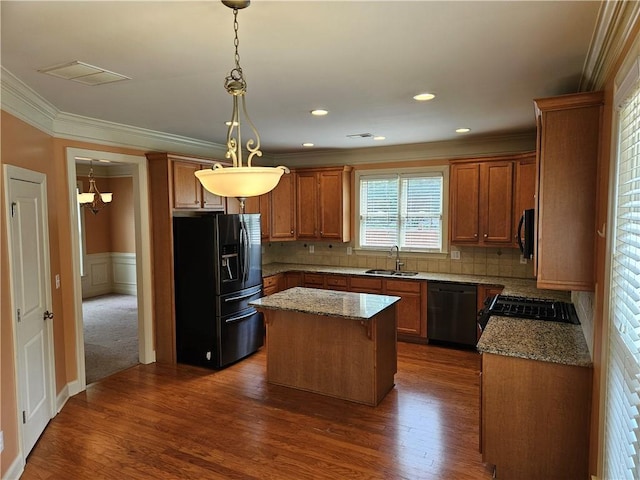 kitchen with a sink, crown molding, visible vents, black appliances, and light stone counters