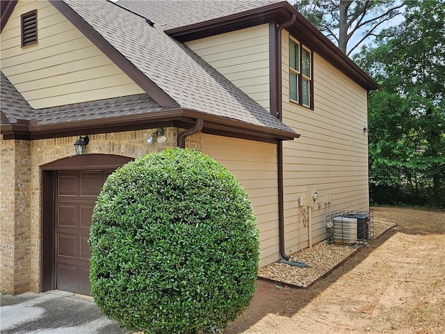 view of side of home featuring a garage, a shingled roof, and central AC