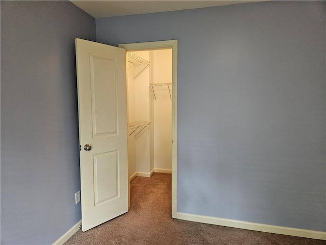 unfurnished bedroom with a spacious closet, carpet floors, baseboards, and a closet