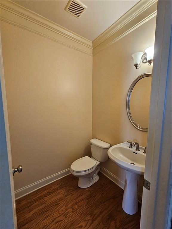 half bathroom featuring toilet, wood finished floors, ornamental molding, visible vents, and baseboards