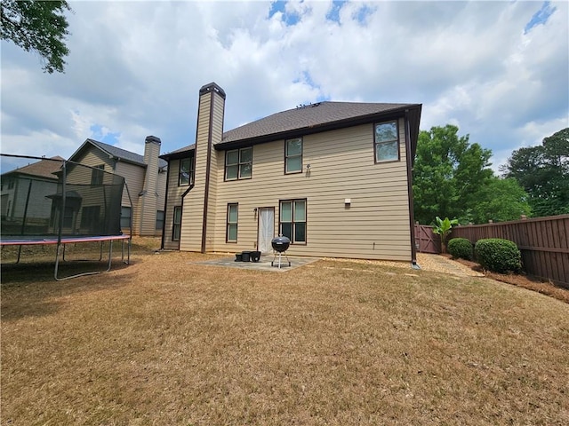 rear view of house with a yard, a chimney, a patio, a trampoline, and a fenced backyard