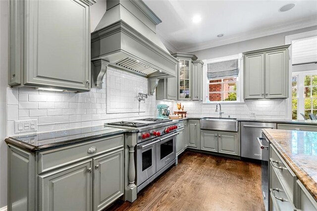kitchen with custom exhaust hood, a sink, dark wood finished floors, appliances with stainless steel finishes, and gray cabinetry