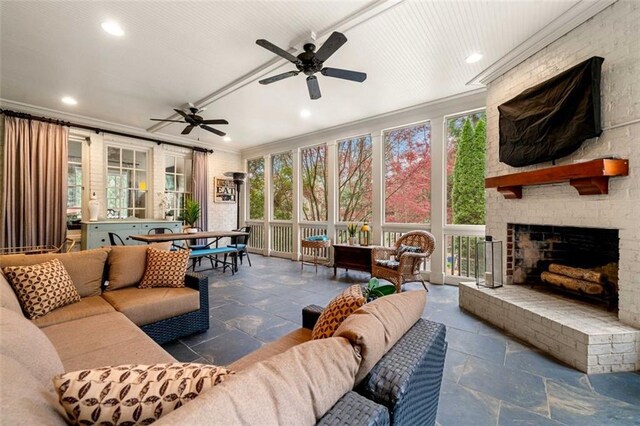 sunroom / solarium with crown molding, a ceiling fan, an outdoor living space with a fireplace, and stone tile floors