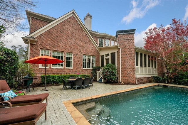back of house with brick siding, a chimney, a patio, and an outdoor pool
