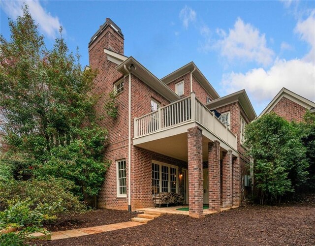 rear view of house featuring brick siding, a chimney, and a balcony