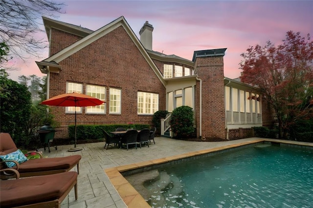 back of house featuring a chimney, a patio area, an outdoor pool, and brick siding