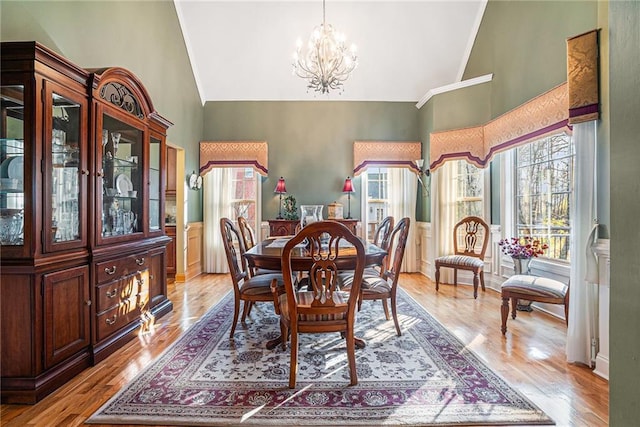 dining space with light wood-type flooring, a wainscoted wall, high vaulted ceiling, and an inviting chandelier