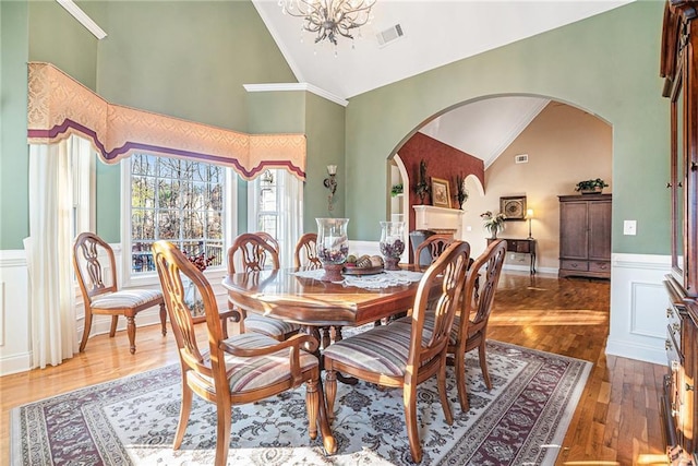 dining space with wood finished floors, visible vents, an inviting chandelier, arched walkways, and wainscoting