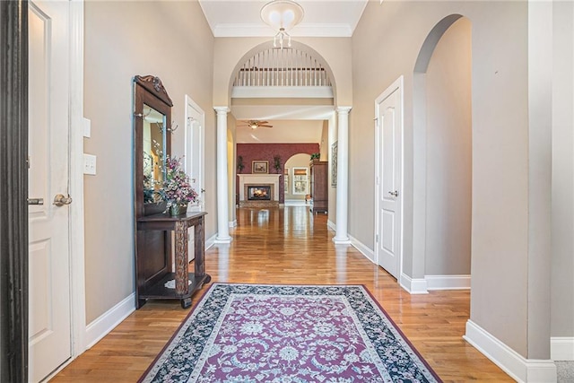 entrance foyer featuring arched walkways, a lit fireplace, light wood finished floors, baseboards, and ornate columns