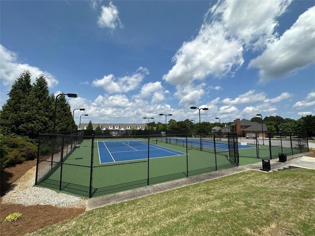 view of tennis court featuring a lawn and fence