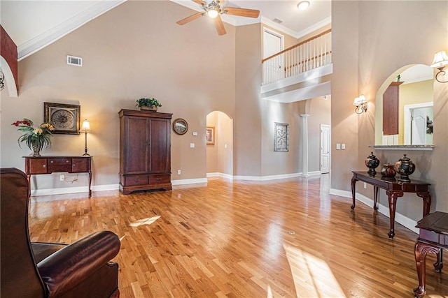 living room with light wood finished floors, visible vents, crown molding, baseboards, and arched walkways