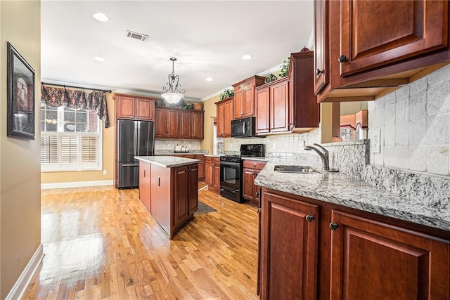 kitchen with visible vents, a kitchen island, light wood-style floors, black appliances, and a sink