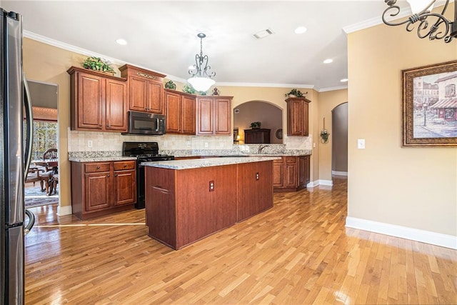 kitchen featuring a kitchen island, tasteful backsplash, gas range oven, freestanding refrigerator, and arched walkways