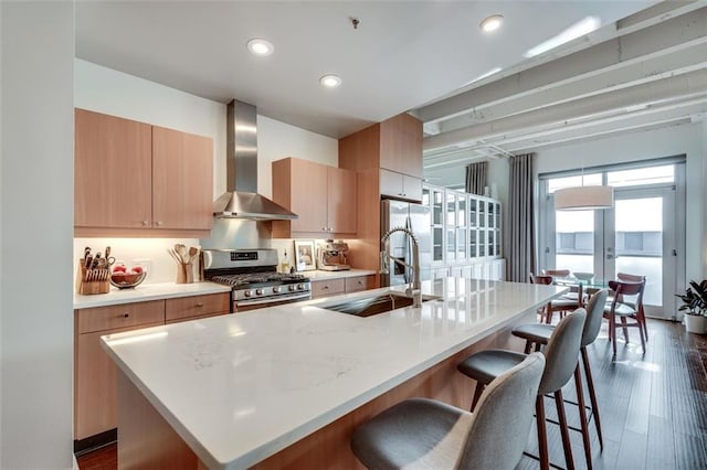 kitchen featuring wall chimney exhaust hood, sink, a center island with sink, appliances with stainless steel finishes, and dark hardwood / wood-style flooring