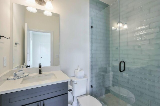 bathroom featuring toilet, vanity, and a shower with shower door