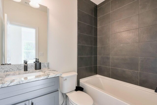 full bathroom featuring vanity, tiled shower / bath combo, and toilet