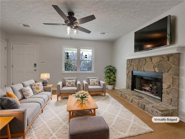 living area with baseboards, visible vents, a fireplace, ceiling fan, and a textured ceiling