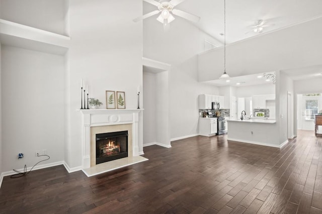 unfurnished living room with sink, a high end fireplace, dark hardwood / wood-style floors, and a high ceiling