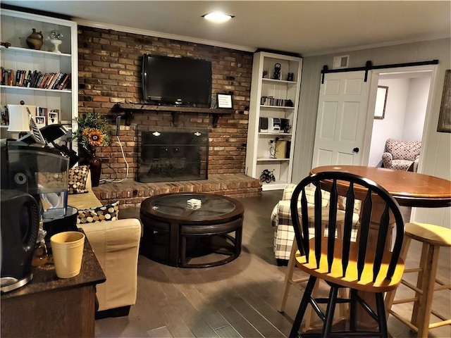 living room with a barn door, built in features, dark hardwood / wood-style flooring, and a brick fireplace