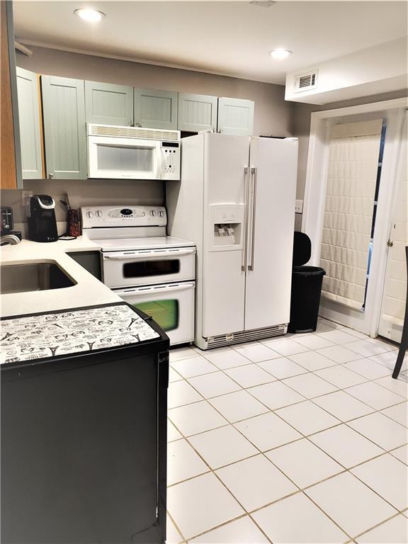 kitchen featuring white appliances, sink, light tile floors, and green cabinets