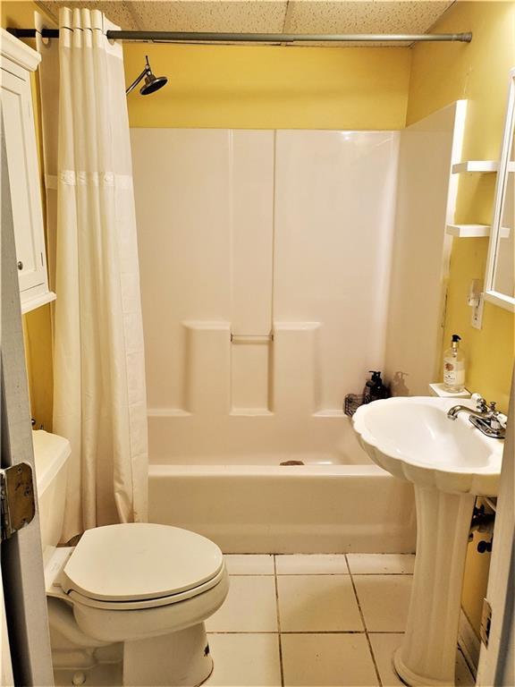 bathroom featuring toilet, shower / tub combo with curtain, and tile floors