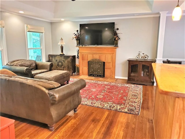 living room with a tiled fireplace, crown molding, a raised ceiling, and hardwood / wood-style flooring