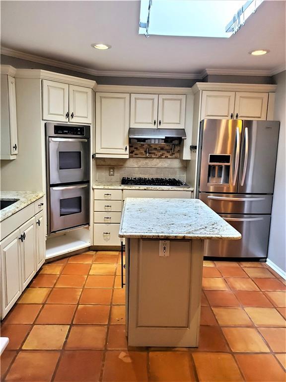 kitchen featuring appliances with stainless steel finishes, light stone counters, a kitchen island, backsplash, and light tile floors