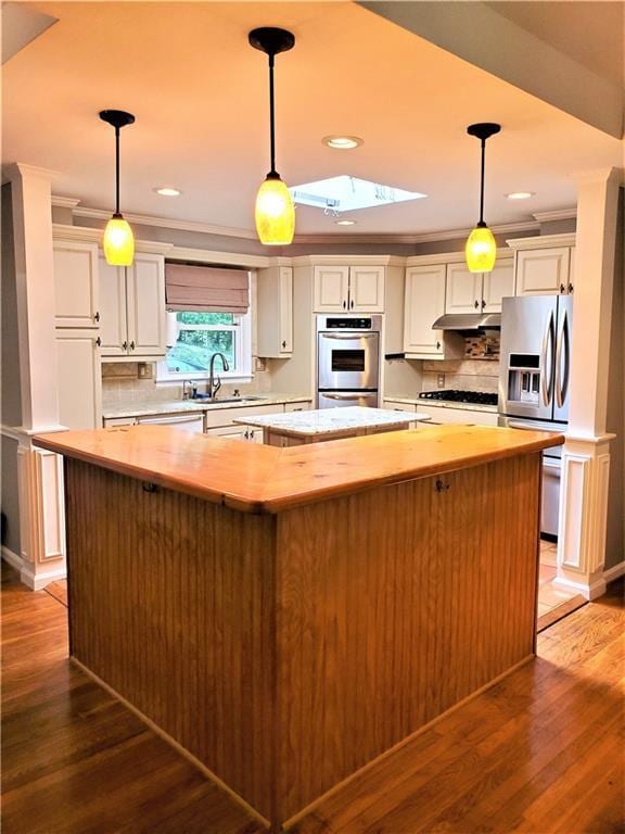 kitchen featuring stainless steel appliances, a kitchen island, decorative light fixtures, tasteful backsplash, and hardwood / wood-style floors