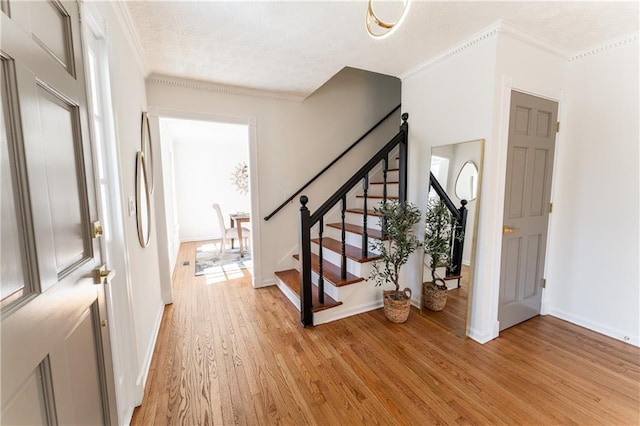 foyer featuring baseboards, stairway, ornamental molding, a textured ceiling, and light wood-style floors