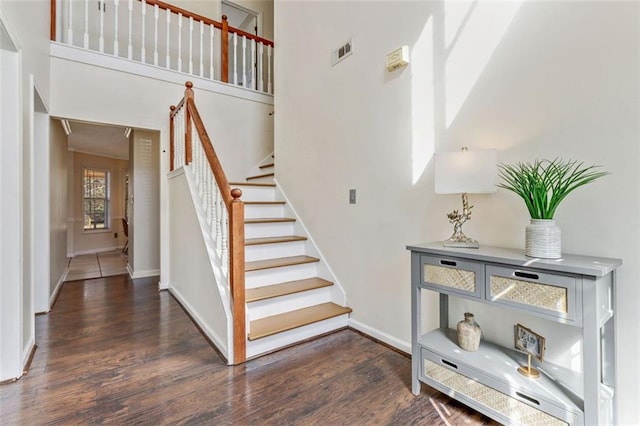 staircase featuring visible vents, a towering ceiling, baseboards, and wood finished floors