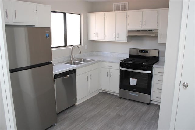 kitchen with appliances with stainless steel finishes, sink, white cabinets, and light wood-type flooring