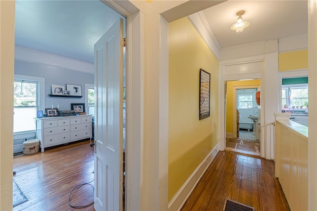 hallway with baseboards, wood-type flooring, ornamental molding, and visible vents