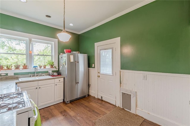 kitchen featuring ornamental molding, freestanding refrigerator, a wainscoted wall, white cabinets, and a sink