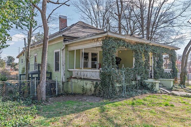 view of front of home featuring roof with shingles, a chimney, a front yard, fence, and covered porch