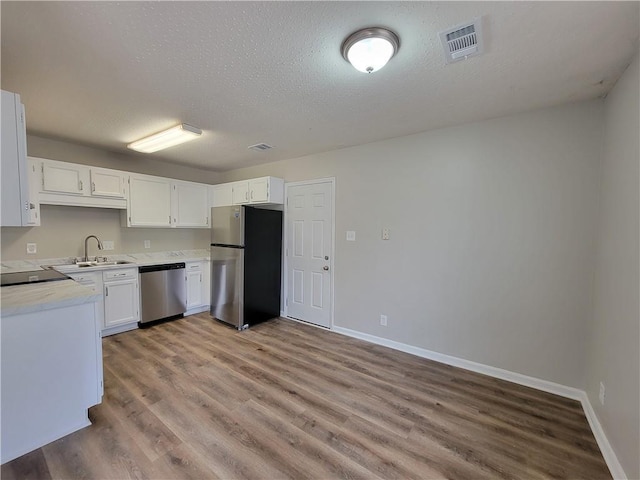 kitchen with sink, a textured ceiling, light wood-type flooring, appliances with stainless steel finishes, and white cabinets