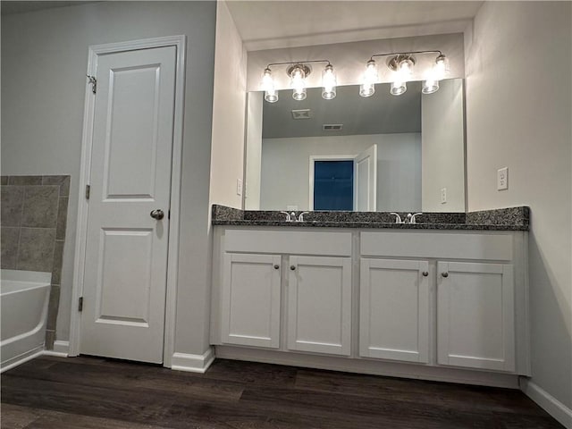 full bath with double vanity, wood finished floors, baseboards, and a bathtub