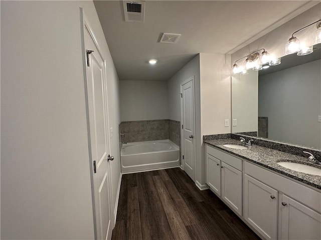 bathroom with wood finished floors, double vanity, and a bath