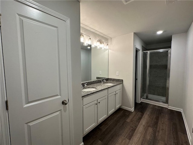 bathroom with wood finished floors, a shower stall, baseboards, and double vanity