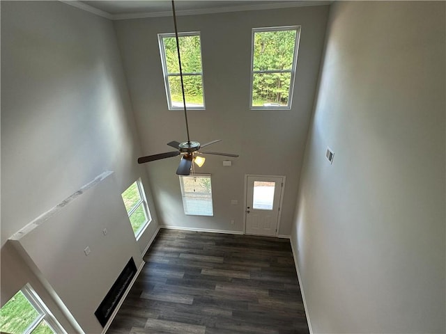 unfurnished living room featuring plenty of natural light, dark wood finished floors, a ceiling fan, a towering ceiling, and crown molding