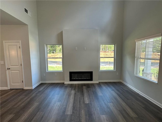 unfurnished living room with a high ceiling, healthy amount of natural light, dark wood finished floors, and baseboards