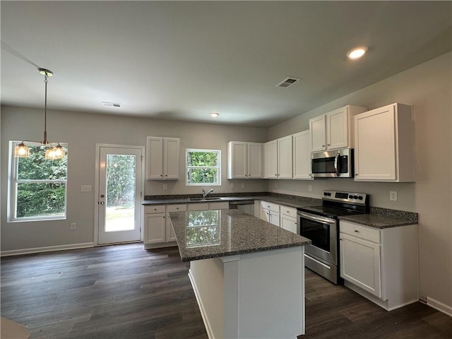 kitchen with stainless steel appliances, a sink, white cabinetry, dark wood-style floors, and a center island