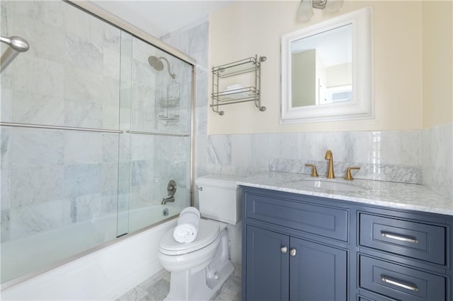 full bath with a wainscoted wall, toilet, tile walls, enclosed tub / shower combo, and vanity