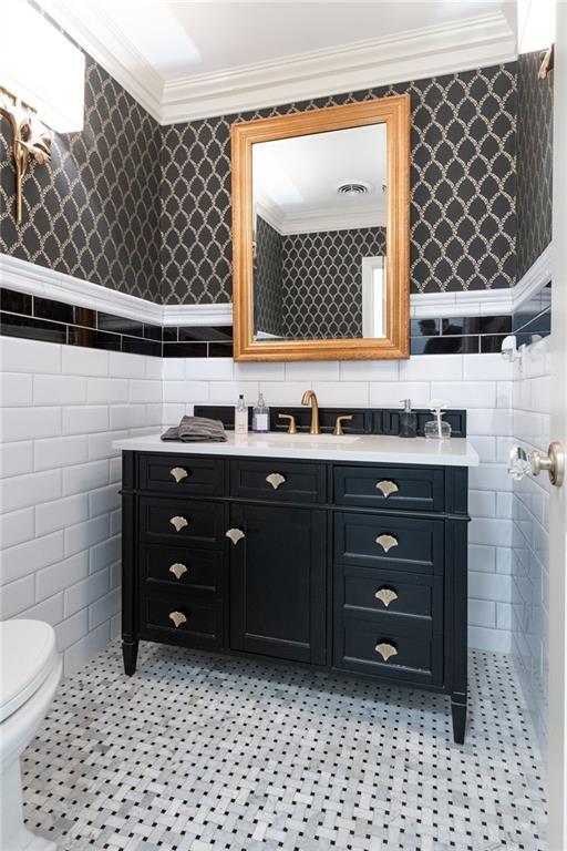 bathroom featuring visible vents, a wainscoted wall, crown molding, wallpapered walls, and vanity