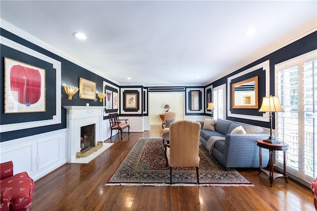 living room with wood finished floors, a fireplace with raised hearth, crown molding, and a decorative wall