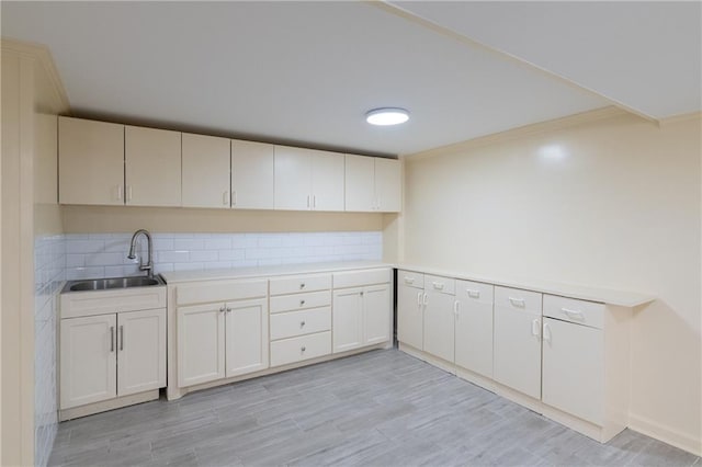 kitchen featuring light wood finished floors, backsplash, crown molding, light countertops, and a sink