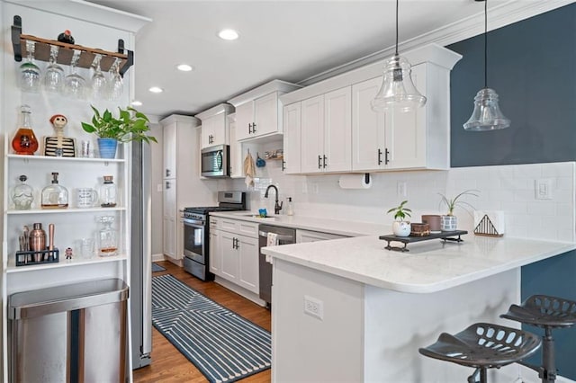 kitchen with pendant lighting, a breakfast bar area, white cabinetry, stainless steel appliances, and kitchen peninsula