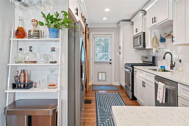 kitchen with appliances with stainless steel finishes, white cabinetry, sink, ornamental molding, and a barn door